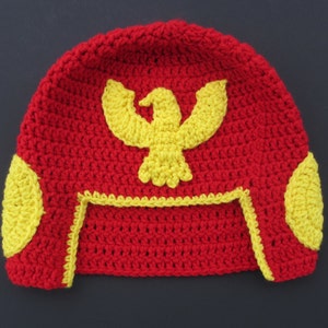 May include: Red crocheted hat with a yellow eagle design and yellow accents on the sides.