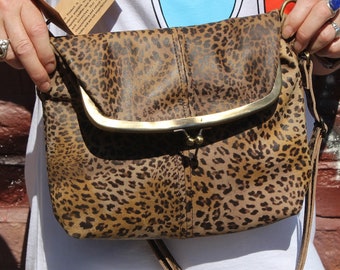 May include: A brown and black leopard print leather purse with a gold clasp and a long strap. The purse is being held by a person.