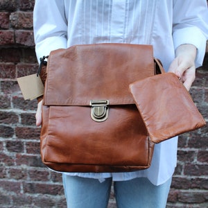 Puede incluir: Una mochila de cuero marrón con cierre de solapa y una bolsa de cuero marrón a juego. La mochila tiene una hebilla de latón y una correa.