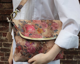 May include: A floral patterned leather handbag with a brass clasp and a long strap. The bag is a light brown colour with pink, red, and yellow flowers.