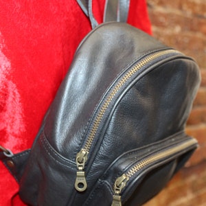 Pode incluir: Uma mochila de couro preto com zíperes dourados e um pequeno bolso na frente.