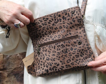 May include: A brown leather crossbody bag with a leopard print design. The bag has a zippered pocket and a flap closure.
