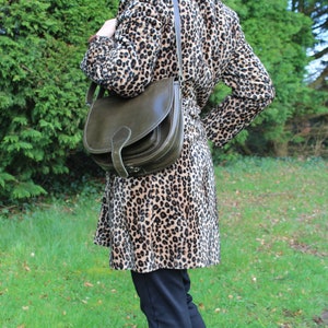 May include: A woman wearing a brown and black leopard print coat with a dark green leather satchel bag.