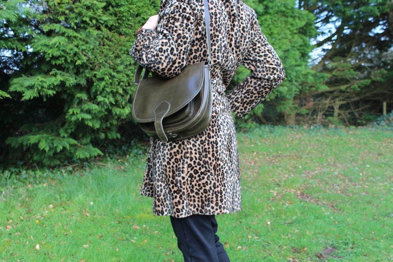 May include: A woman wearing a brown and black leopard print coat with a dark green leather satchel bag.