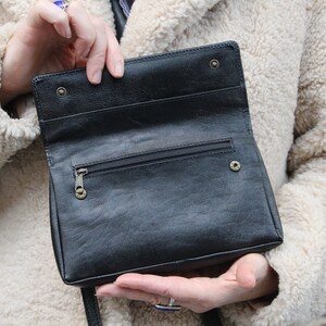 K&ouml;nnte beinhalten: Eine schwarze Lederhandtasche mit einem Rei&szlig;verschlussfach und einem Klappverschluss. Die Tasche ist offen und das Innere ist sichtbar.