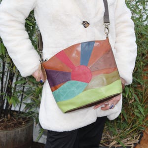 Può includere: Una borsa a tracolla in pelle multicolore con un design di alba. La borsa è realizzata in diverse tonalità di pelle marrone, rosso, verde, blu e viola. La borsa ha una tracolla lunga e una chiusura a lembo.