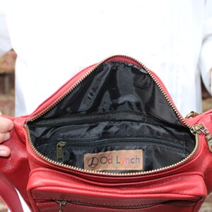 Puede incluir: Ri&ntilde;onera de cuero rojo con cierre de cremallera y hebilla de metal dorado. El interior de la bolsa est&aacute; forrado con tela negra y tiene un bolsillo peque&ntilde;o. La bolsa tiene una etiqueta que dice "OodLynch".