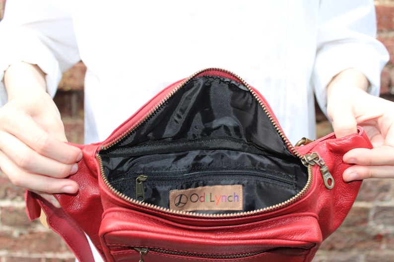 Puede incluir: Ri&ntilde;onera de cuero rojo con cierre de cremallera y hebilla de metal dorado. El interior de la bolsa est&aacute; forrado con tela negra y tiene un bolsillo peque&ntilde;o. La bolsa tiene una etiqueta que dice "OodLynch".