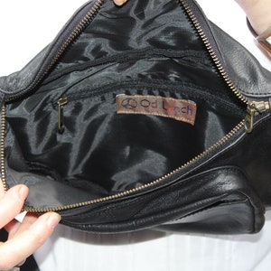 May include: Black leather fanny pack with a zippered main compartment and a smaller front pocket. The interior is lined with black fabric and features a small leather tag with the text "Od Lynch". The bag has a gold-colored zipper.