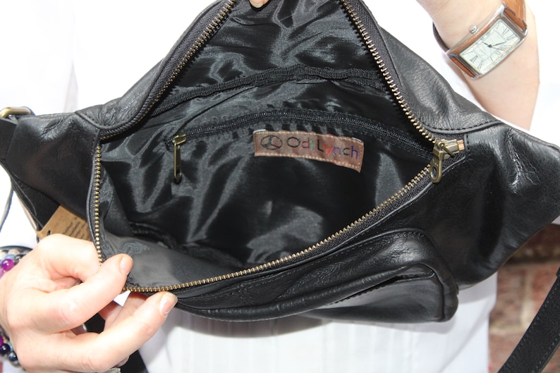 May include: Black leather fanny pack with a zippered main compartment and a smaller front pocket. The interior is lined with black fabric and features a small leather tag with the text "Od Lynch". The bag has a gold-colored zipper.