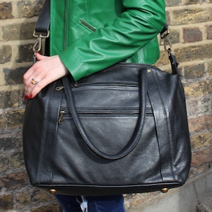 Może przedstawiać: Czarna skórzana torba typu tote z wieloma kieszeniami i długim paskiem. Torba ma zamek błyskawiczny i złote okucia.