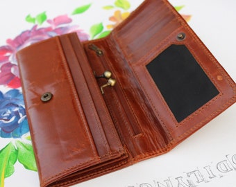May include: A brown leather wallet with multiple compartments and a zipped pocket. The wallet is open to reveal a black fabric interior with a card slot.
