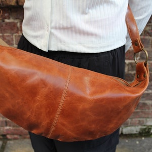 May include: A brown leather crossbody bag with a zipper closure and a metal ring on the strap.
