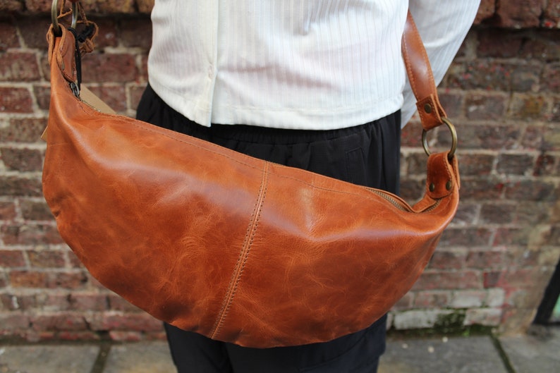 May include: A brown leather crossbody bag with a zipper closure and a metal ring on the strap.