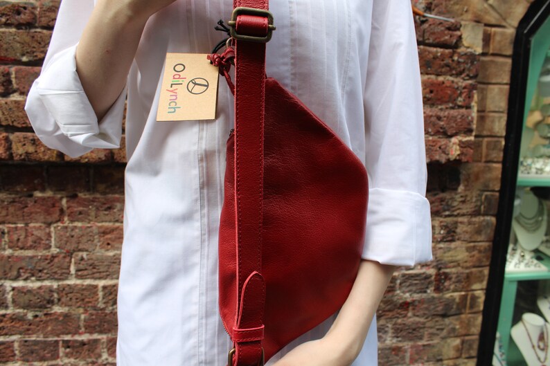 Puede incluir: Un bolso bandolera de cuero rojo con una correa marr&oacute;n y una peque&ntilde;a etiqueta marr&oacute;n que dice "odiLynch".