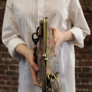 May include: A vintage-style floral patterned clutch purse with a brass clasp and chain strap.