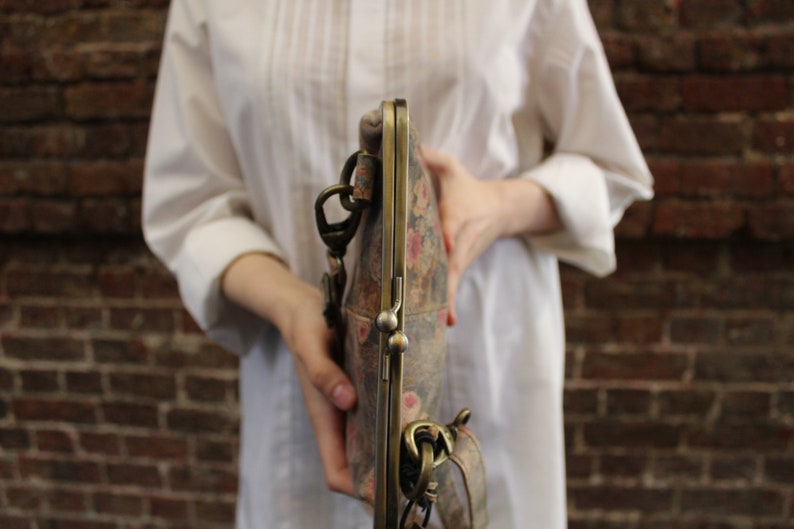 May include: A vintage-style floral patterned clutch purse with a brass clasp and chain strap.