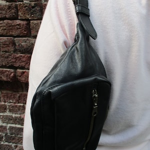 May include: A black leather fanny pack with a zippered pocket and a long adjustable strap. The strap has a metal buckle.