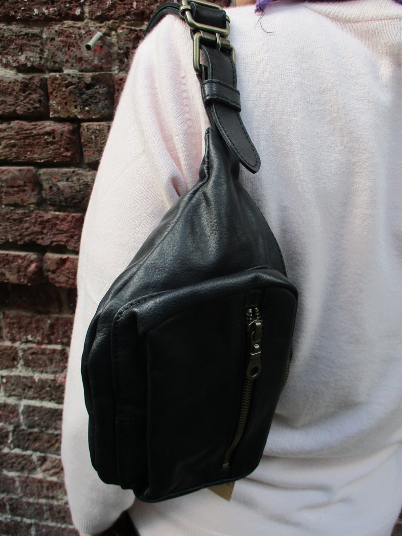 May include: A black leather fanny pack with a zippered pocket and a long adjustable strap. The strap has a metal buckle.