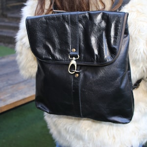 May include: A black leather backpack with a flap closure and a gold hook. The backpack has a zipper on the front and a strap on the side.