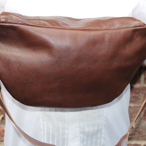 K&ouml;nnte beinhalten: Eine braune Leder-Bauchtasche mit einem langen verstellbaren Riemen. Die Tasche hat ein Etikett mit der Aufschrift "odiLynch" und einem stilisierten Vogel-Logo.