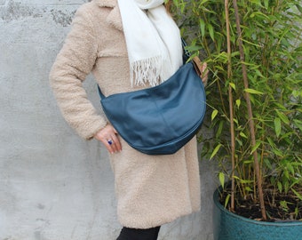 May include: A woman wearing a cream-colored fuzzy coat and a white scarf is carrying a teal blue leather shoulder bag.