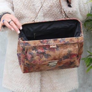May include: A vintage-style handbag with a floral pattern in shades of brown, red, and pink. The bag has a rectangular shape, a metal clasp, and a black interior. It features a front pocket and a shoulder strap.
