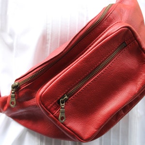 Puede incluir: Una ri&ntilde;onera de cuero roja con dos compartimentos con cremallera. La bolsa se lleva en la cintura.