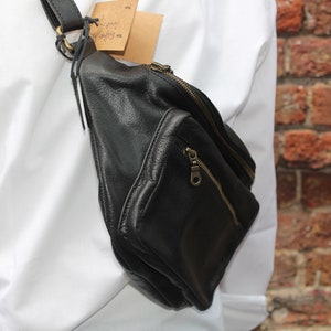 May include: Black leather fanny pack with a zippered main compartment and a smaller front pocket. The bag has a black strap and gold-colored zippers. A small tag is attached to the strap.