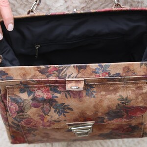 May include: A vintage handbag featuring a floral design in brown, red, and green hues. The rectangular bag has a front pocket and a silver clasp. The interior is black, and it has a silver chain handle. The bag's design evokes a classic aesthetic.