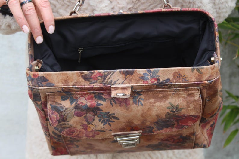 May include: A vintage handbag featuring a floral design in brown, red, and green hues. The rectangular bag has a front pocket and a silver clasp. The interior is black, and it has a silver chain handle. The bag's design evokes a classic aesthetic.