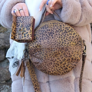 May include: A brown and tan leopard print round purse with a matching smaller wallet. The purse has a long strap and a zipper closure.