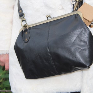 May include: A black leather crossbody bag with a brass clasp and a long strap. The bag is worn over a white faux fur jacket.