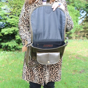 May include: A green leather satchel bag with a flap closure and a small front pocket. The bag is open and the inside is lined with black fabric.
