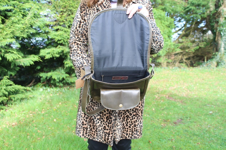 May include: A green leather satchel bag with a flap closure and a small front pocket. The bag is open and the inside is lined with black fabric.