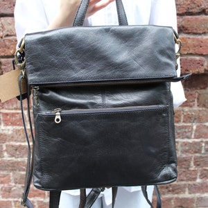 May include: Black leather backpack with a flap closure and a zipped pocket on the front. The backpack has adjustable straps and a top handle.