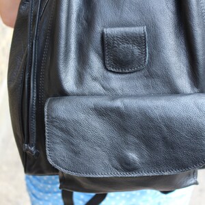 May include: A black leather backpack with a large front pocket and a smaller pocket above it. The backpack has a drawstring closure.