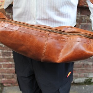 May include: A brown leather crossbody bag with a zipper closure. The bag is curved and has a long strap.