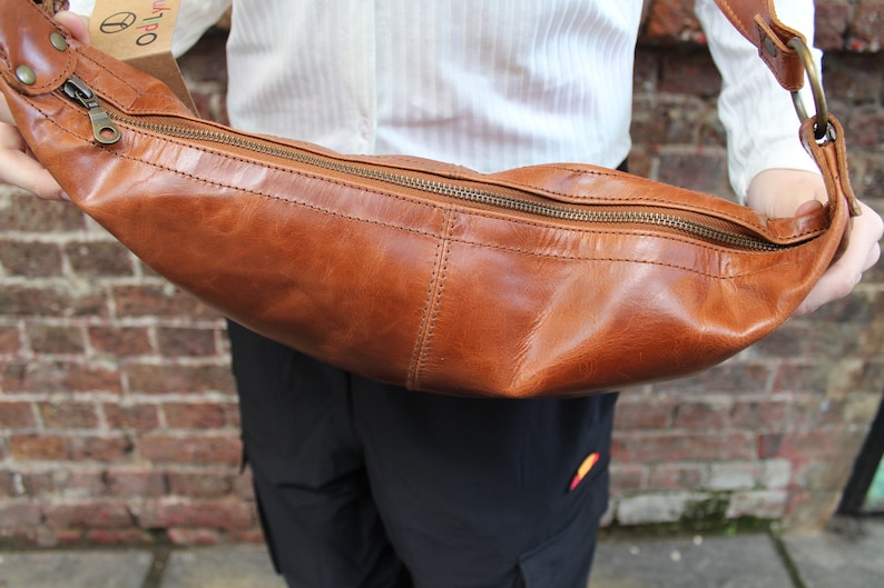 May include: A brown leather crossbody bag with a zipper closure. The bag is curved and has a long strap.