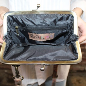 May include: A black fabric purse with a gold metal frame and a zippered pocket. The purse has a small label inside that says "Odd Lynch" with a peace sign.