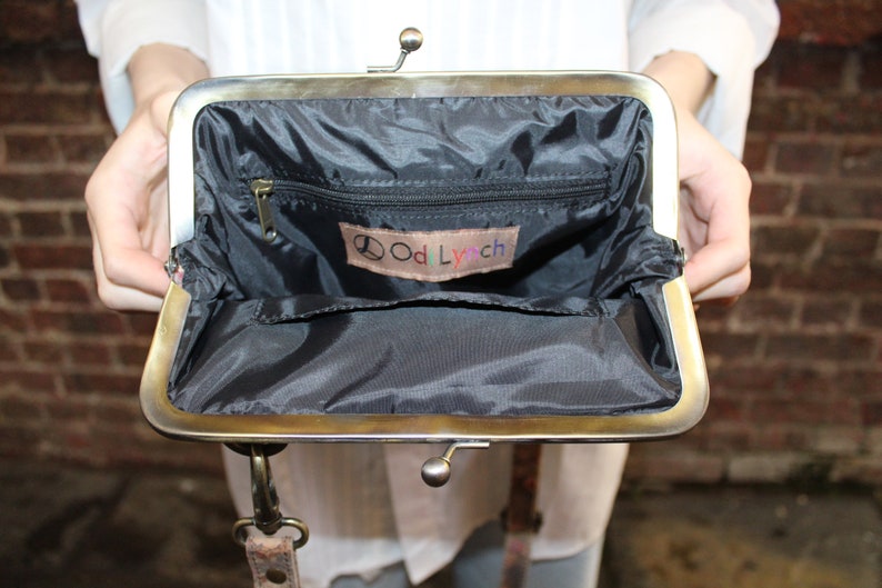 May include: A black fabric purse with a gold metal frame and a zippered pocket. The purse has a small label inside that says "Odd Lynch" with a peace sign.