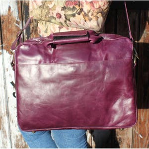 Könnte beinhalten: Eine dunkelviolette Ledertasche mit einem Tragegriff oben und einem Schultergurt. Die Tasche hat einen Klappverschluss und eine Fronttasche.