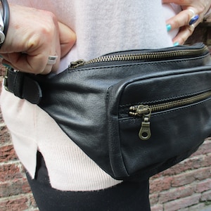 May include: Black leather fanny pack with a zippered pocket and a buckle closure. The fanny pack is worn around the waist.