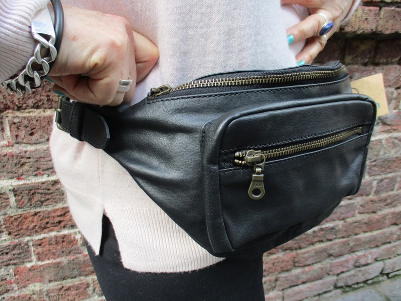 May include: Black leather fanny pack with a zippered pocket and a buckle closure. The fanny pack is worn around the waist.
