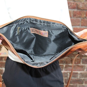 May include: A brown leather crossbody bag with a zipper closure and a black fabric lining. The bag has a small zippered pocket inside and a label that reads "Dod Lynch".
