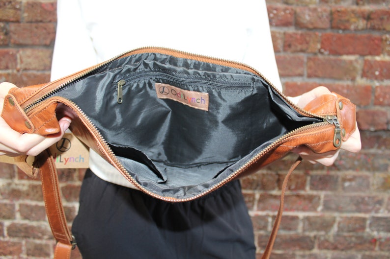 May include: A brown leather crossbody bag with a zipper closure and a black fabric lining. The bag has a small zippered pocket inside and a label that reads "Dod Lynch".