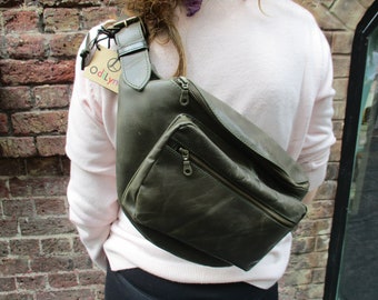 May include: A dark green leather fanny pack with a zippered pocket and a buckle strap. The bag is worn on a person's waist.