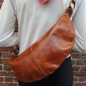 May include: A brown leather fanny pack with a metal buckle and strap. The bag is worn on a person's waist.