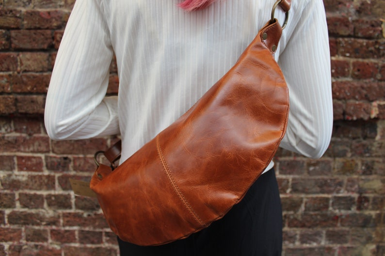May include: A brown leather fanny pack with a metal buckle and strap. The bag is worn on a person's waist.