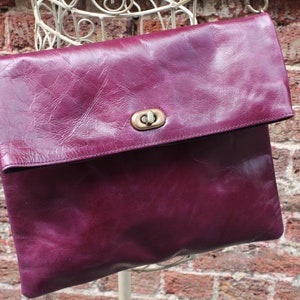 May include: A deep purple leather crossbody bag with a flap closure and a gold metal clasp.